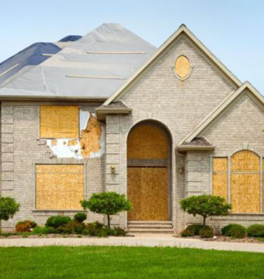 House that has been boarded up and tarped over after heavy damage. 